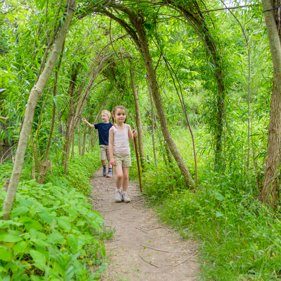 Two young white children walking through the willow tunnel in the Nature PlayScape
